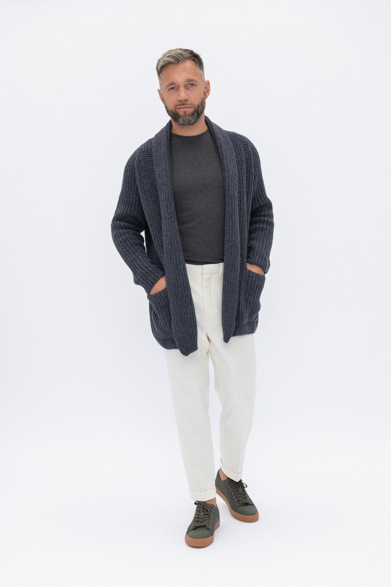 May include: A man wearing a dark blue cardigan over a gray t-shirt, white pants, and dark green sneakers.
