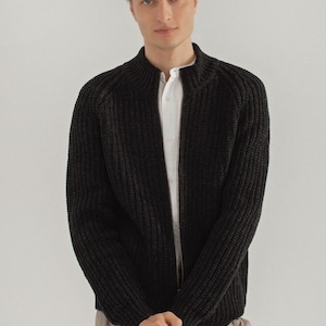 Pu&ograve; includere: Un cardigan nero in maglia con zip e collo alto.
