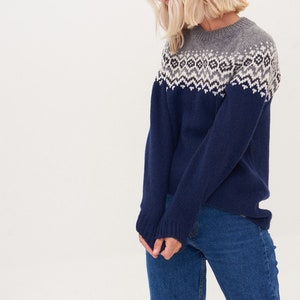May include: A navy blue sweater with a white and gray geometric pattern around the neckline. The sweater is made of a soft, knitted fabric.