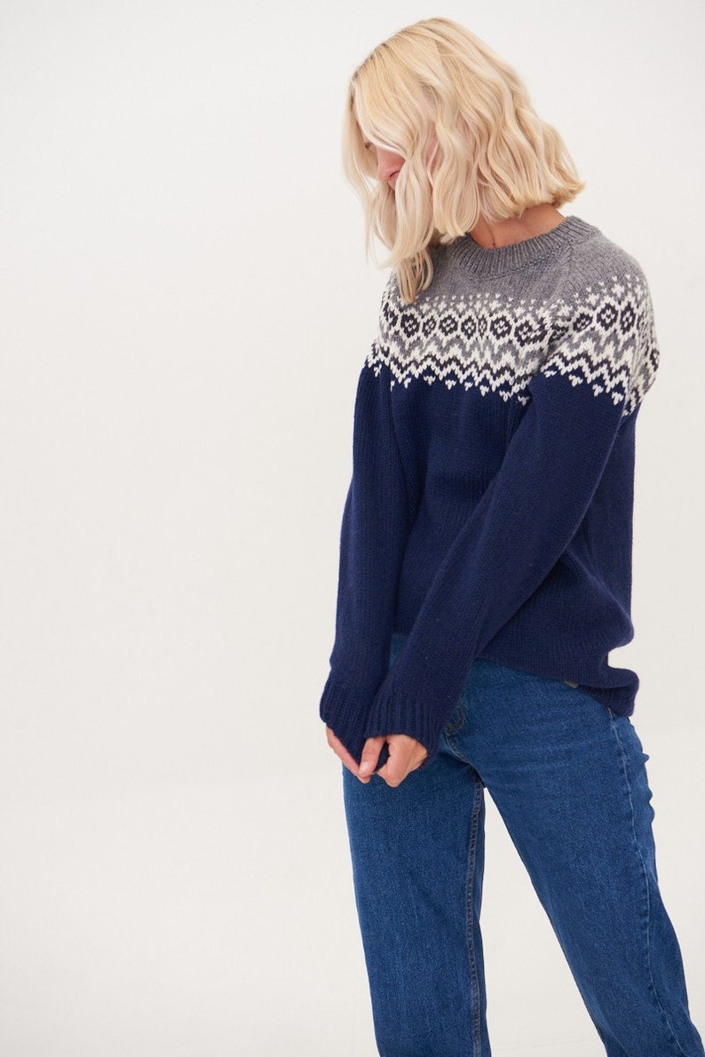 May include: A navy blue sweater with a white and gray geometric pattern around the neckline. The sweater is made of a soft, knitted fabric.