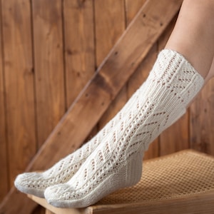May include: A pair of white knitted socks with a lacy pattern, resting on a wooden chair with a woven seat.