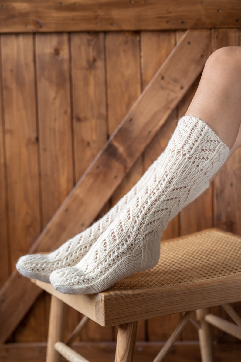 May include: A pair of white knitted socks with a lacy pattern, resting on a wooden chair with a woven seat.