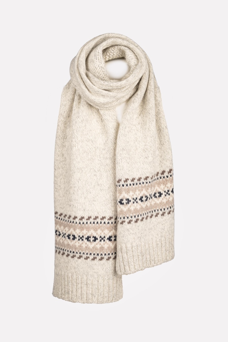 May include: Cream-colored knitted scarf with a geometric pattern in brown, black, and navy blue. The scarf is folded and draped, showcasing its texture and design. A cozy winter accessory.
