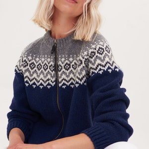 May include: A blue and gray knitted cardigan with a zipper closure and a traditional Scandinavian pattern. The cardigan is made of wool and has a relaxed fit.