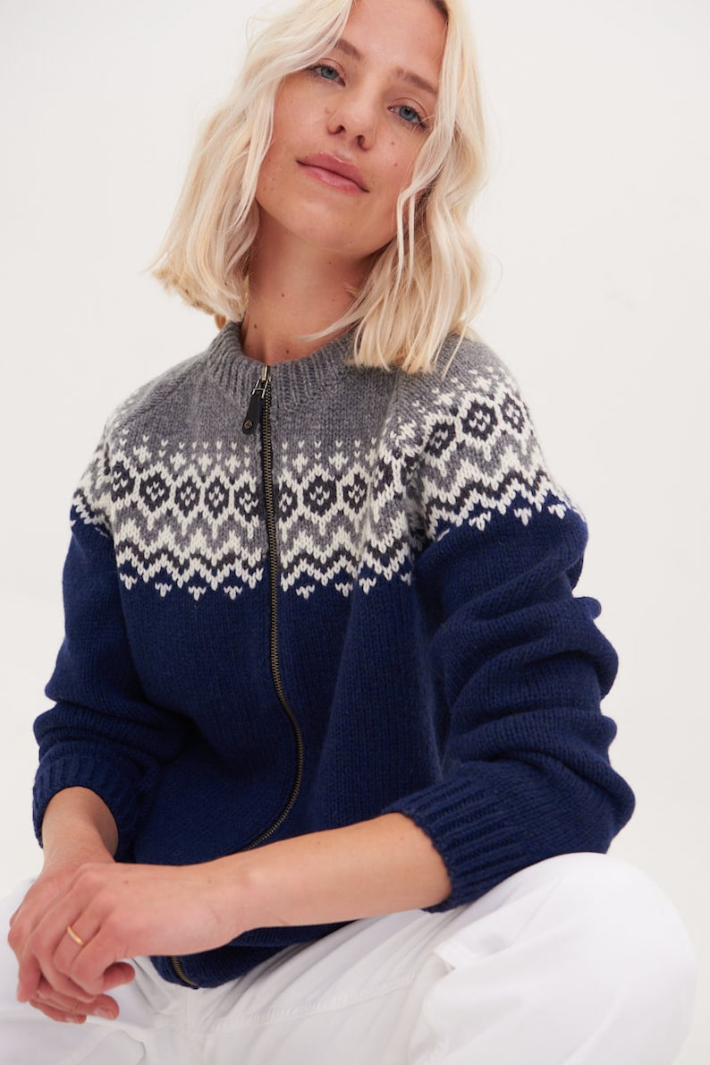 May include: A blue and gray knitted cardigan with a zipper closure and a traditional Scandinavian pattern. The cardigan is made of wool and has a relaxed fit.