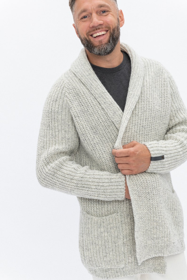 May include: A light gray knitted cardigan with a shawl collar and a single button closure. The cardigan has a patch pocket on the left side and a small black label on the right sleeve.
