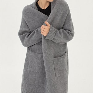 May include: A long, gray cardigan with a shawl collar and two patch pockets. The cardigan is made of a soft, knitted fabric.