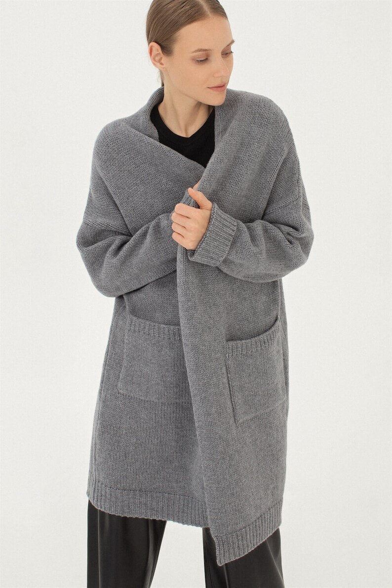May include: A long, gray cardigan with a shawl collar and two patch pockets. The cardigan is made of a soft, knitted fabric.