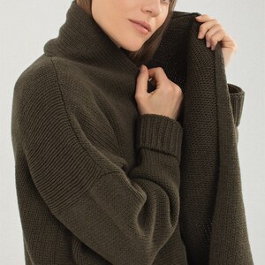 May include: A long-sleeved, dark green cardigan with a shawl collar and a patch pocket. The cardigan is made of a soft, knitted fabric.