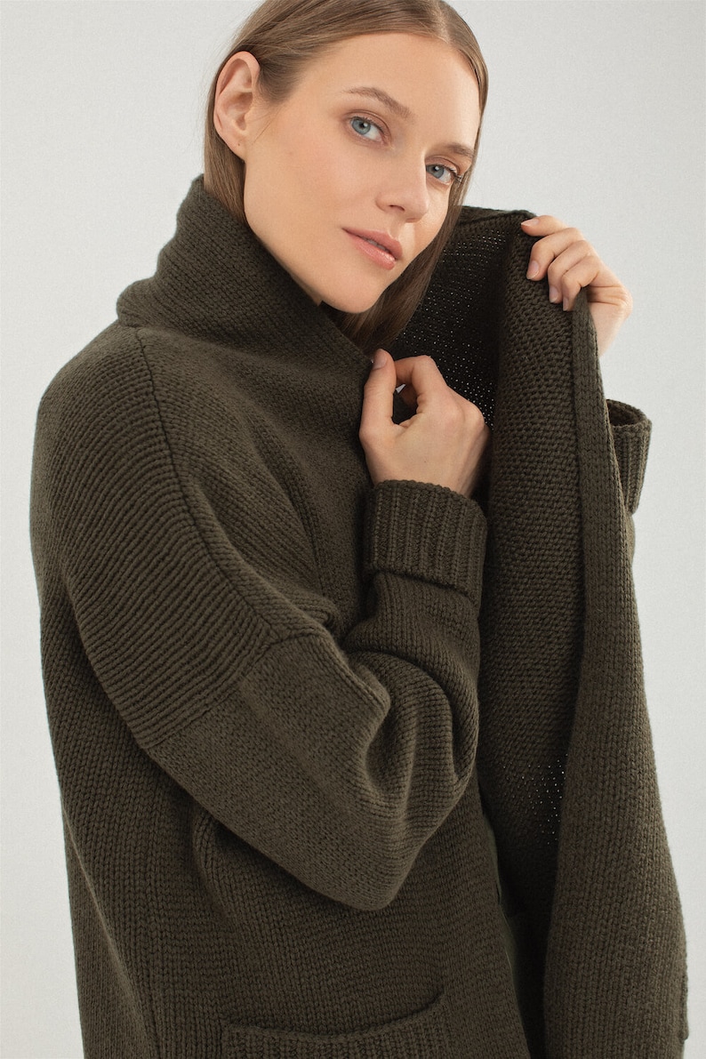May include: A long-sleeved, dark green cardigan with a shawl collar and a patch pocket. The cardigan is made of a soft, knitted fabric.