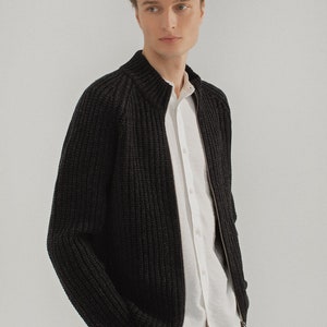May include: A black knitted cardigan with a zipper closure. The cardigan has a ribbed texture and a stand-up collar.