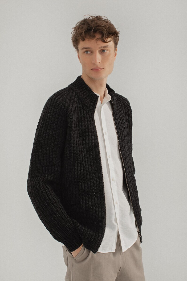 May include: A black knitted cardigan with a zipper closure. The cardigan has a ribbed texture and a stand-up collar.