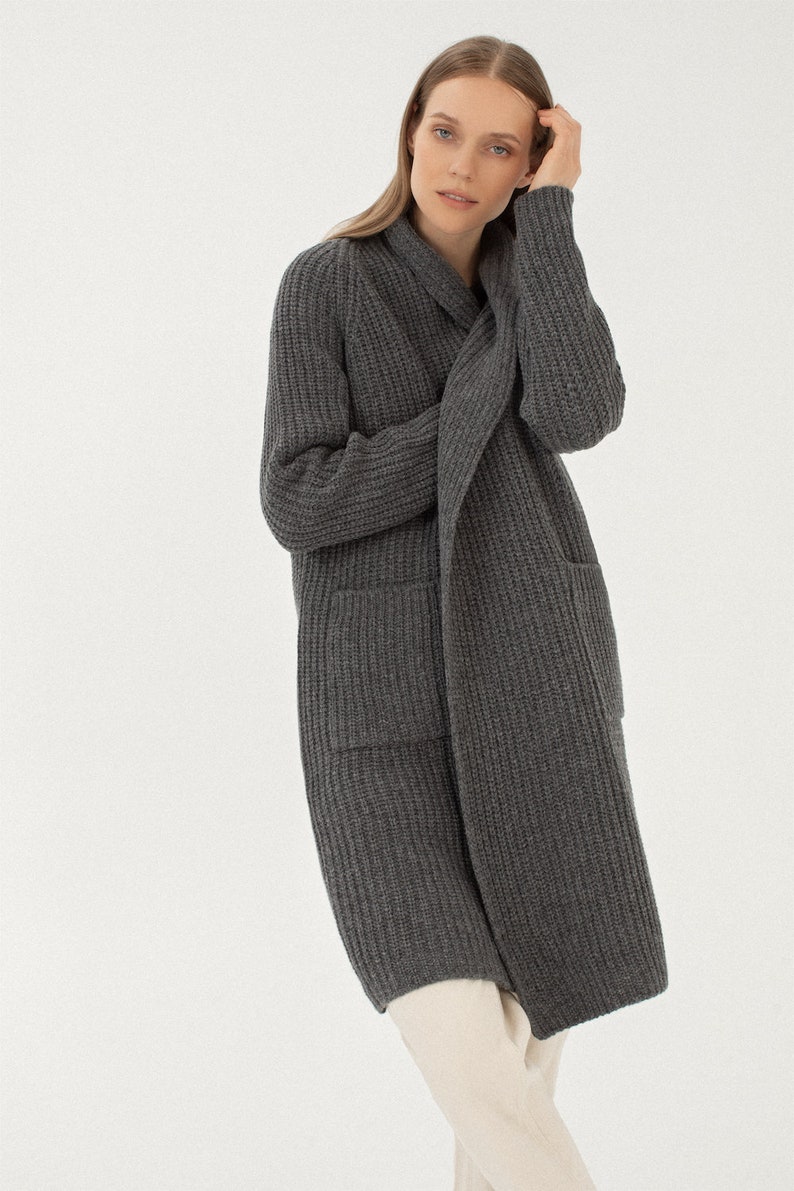 Pu&ograve; includere: Un cardigan lungo di colore grigio con collo a scialle e due tasche. Il cardigan &egrave; realizzato in un tessuto morbido e lavorato a maglia.