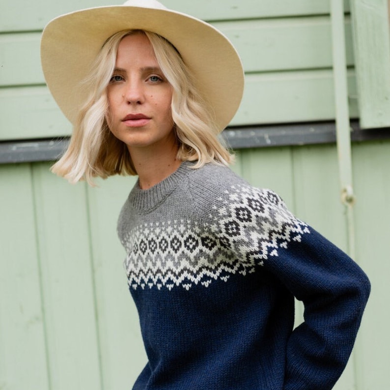 May include: A woman wearing a gray and blue patterned sweater with a white hat. The sweater has a geometric design.