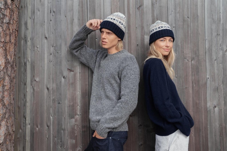 May include: Two people wearing gray and navy blue sweaters with matching patterned knit hats. The hats have a white and gray geometric pattern with a navy blue band.