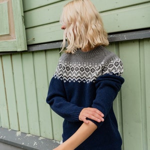 May include: A navy blue sweater with a white and gray geometric pattern around the neck. The sweater is made of a soft, knitted fabric.