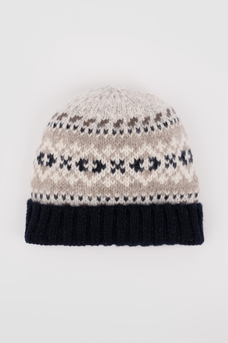 May include: A knitted beanie hat with a navy blue brim and a patterned crown. The crown features a repeating geometric design in light gray, brown, and navy blue. The hat is made of a soft, warm material.