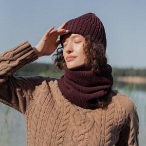 May include: A dark burgundy ribbed knit beanie and a matching dark burgundy ribbed knit neck warmer. The beanie features a folded cuff design, and both items are crafted from a thick, textured yarn, providing a cohesive and warm winter accessory set.
