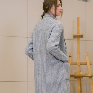 Pu&ograve; includere: Un cardigan lungo di maglia grigia con una trama a coste e una sola tasca sul lato sinistro. Il cardigan &egrave; aperto sul davanti e ha una vestibilit&agrave; rilassata.