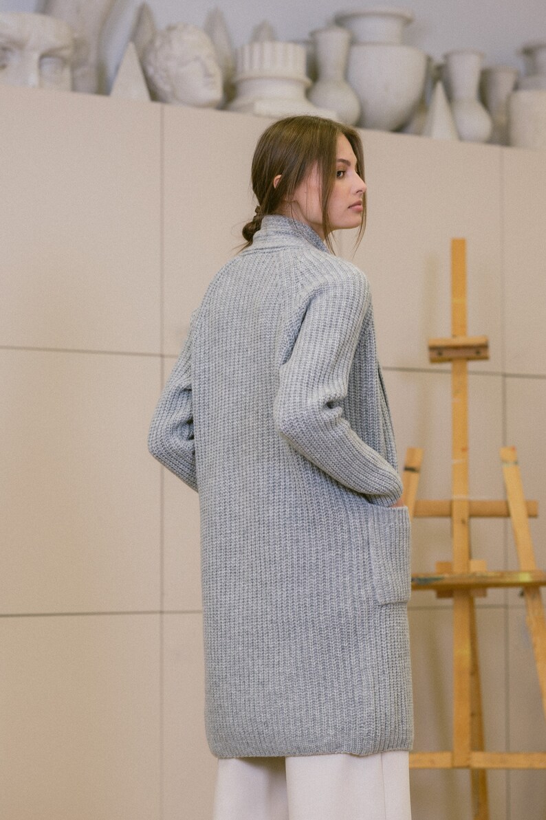 Pu&ograve; includere: Un cardigan lungo di maglia grigia con una trama a coste e una sola tasca sul lato sinistro. Il cardigan &egrave; aperto sul davanti e ha una vestibilit&agrave; rilassata.