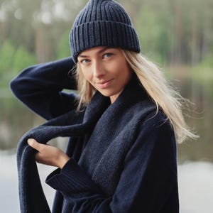 May include: A dark navy blue ribbed knit beanie hat paired with a matching dark navy blue ribbed knit scarf. The beanie features a folded cuff design and a vertical ribbed texture, while the long scarf displays a consistent ribbed knit pattern.