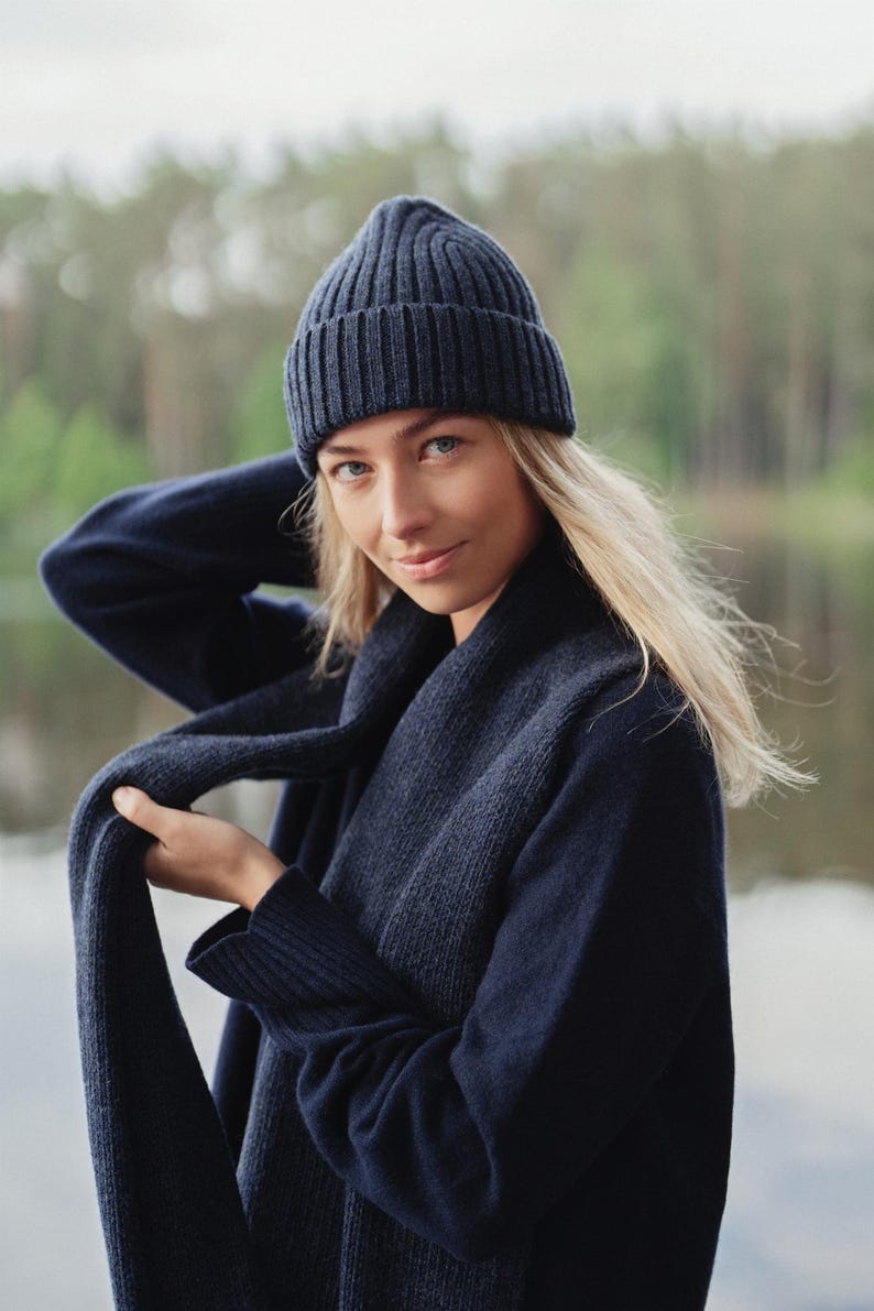 May include: A dark navy blue ribbed knit beanie hat paired with a matching dark navy blue ribbed knit scarf. The beanie features a folded cuff design and a vertical ribbed texture, while the long scarf displays a consistent ribbed knit pattern.