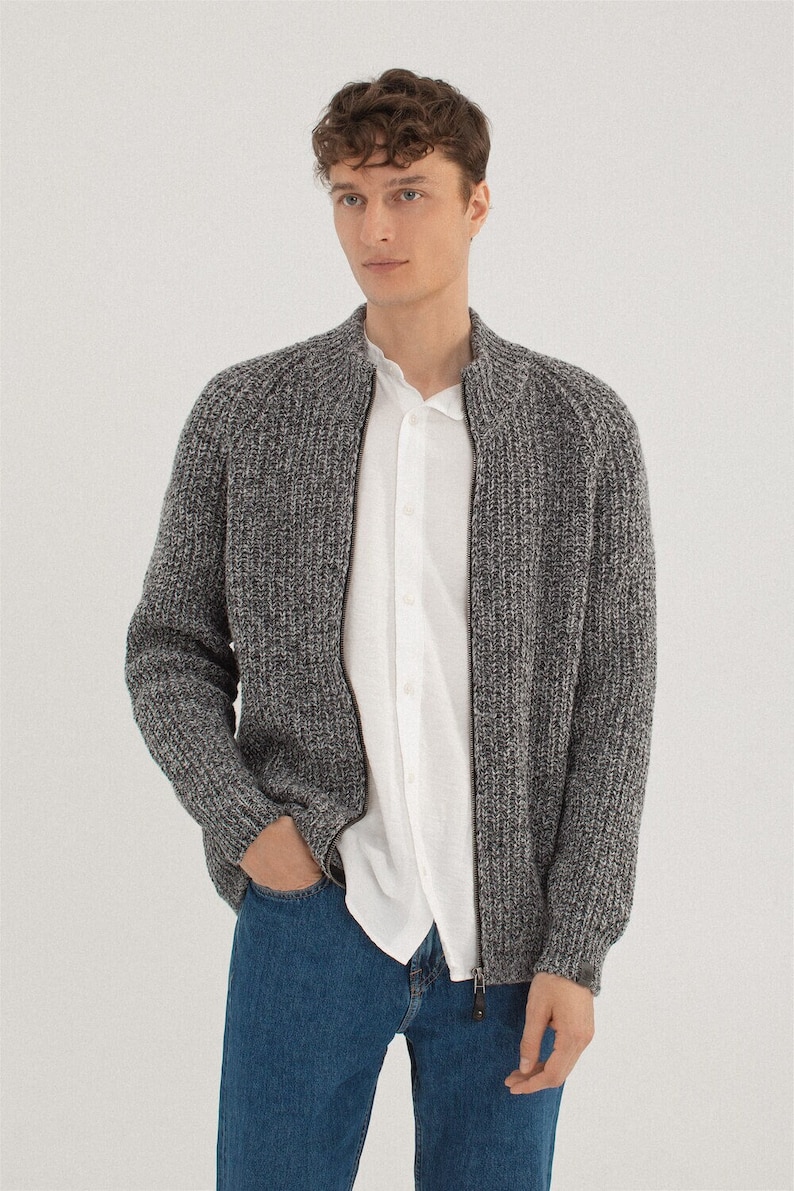 May include: A gray and white knit cardigan with a zipper closure. The cardigan has a textured knit pattern and a stand-up collar.