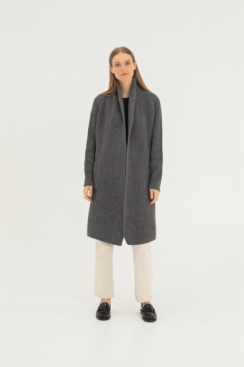 Pu&ograve; includere: Un cardigan lungo di colore grigio con collo a scialle e una tasca a toppa sul lato sinistro. Il cardigan &egrave; realizzato in un tessuto morbido e lavorato a maglia.