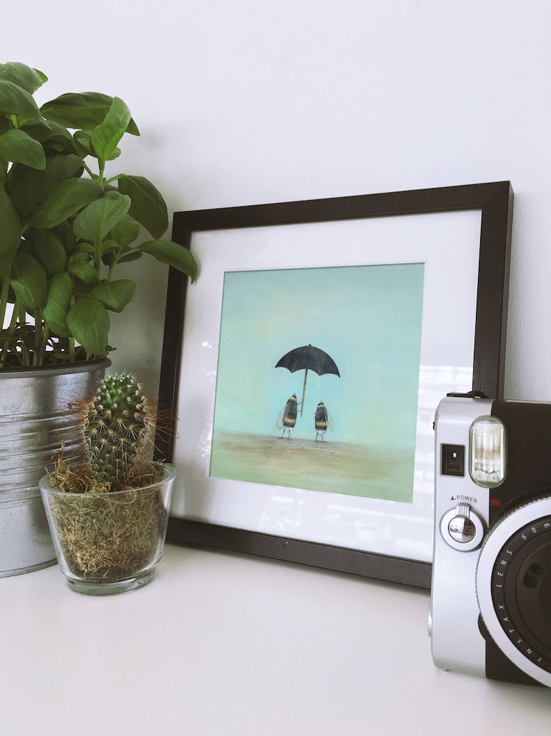 May include: A framed print of a painting depicting two bumblebees walking under a black umbrella on a light blue background.