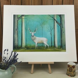 Pode incluir: Um veado branco est&aacute; em uma floresta nebulosa com &aacute;rvores altas e um fundo azul esverdeado. O veado est&aacute; olhando para a frente com seus chifres levantados. A pintura &eacute; emoldurada com um passe-partout branco.