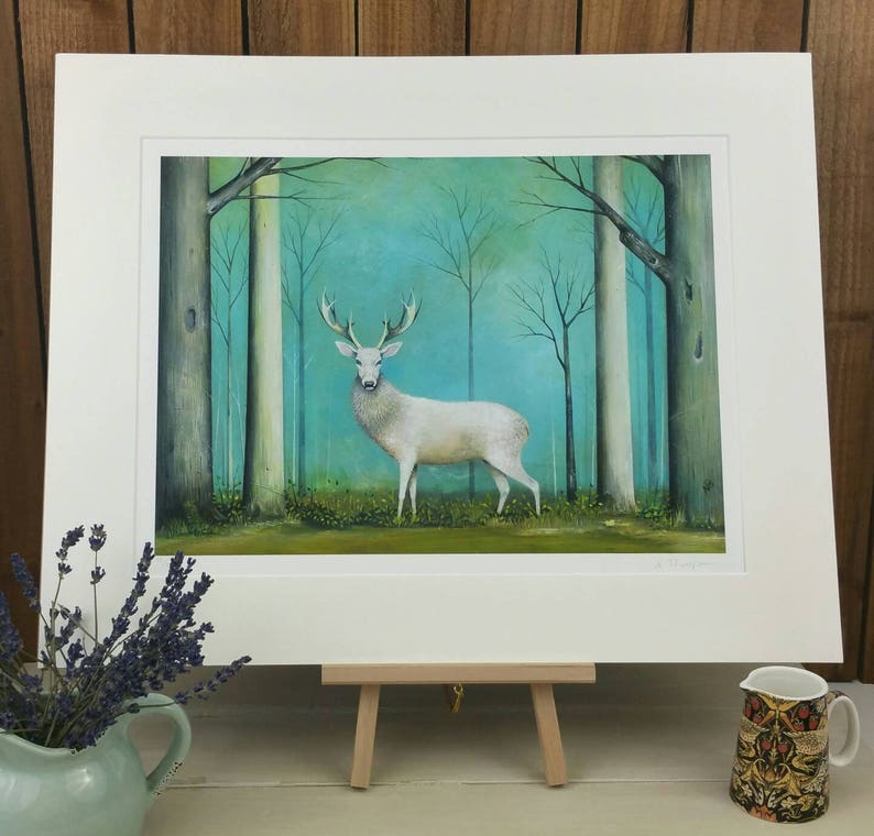 Pode incluir: Um veado branco est&aacute; em uma floresta nebulosa com &aacute;rvores altas e um fundo azul esverdeado. O veado est&aacute; olhando para a frente com seus chifres levantados. A pintura &eacute; emoldurada com um passe-partout branco.