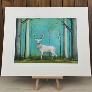 Pode incluir: Um veado branco est&aacute; em uma floresta com um fundo azul-esverdeado. O veado tem grandes chifres e est&aacute; rodeado de &aacute;rvores com galhos nus. A pintura &eacute; emoldurada com uma moldura branca.