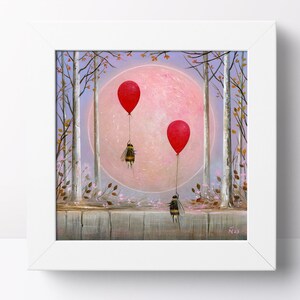 May include: Framed artwork depicting three bees suspended by red balloons in a forest setting. A large pink moon is visible in the background, along with trees and a wooden fence. The artwork is presented within a white frame.