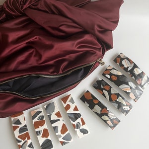 May include: Five hair clips with a terrazzo pattern. The clips are in two different color schemes: black and white, and brown, white, and gray. The clips are arranged in a row on a white surface.
