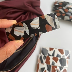 May include: A set of four black and white hair clips with a terrazzo pattern. The clips are made of resin and have a glossy finish.