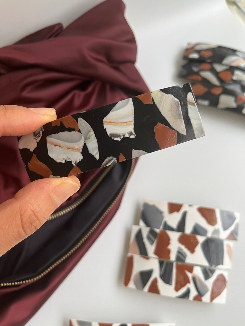 May include: A set of four black and white hair clips with a terrazzo pattern. The clips are made of resin and have a glossy finish.
