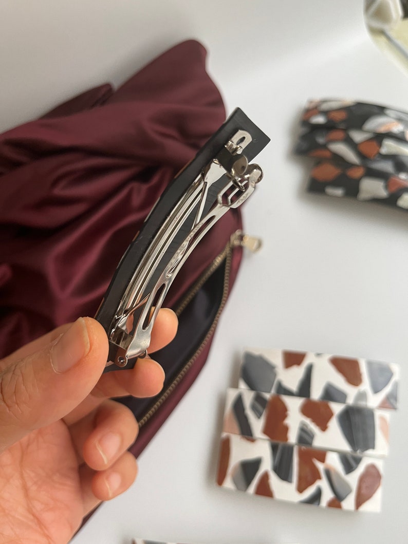 May include: A silver metal hair clip with a black plastic base. The clip is open and ready to be used to hold hair in place.