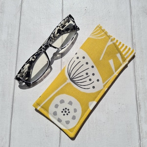 May include: A yellow glasses case with a white floral pattern. The case is made of fabric and has a zipper closure.