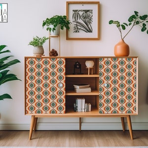 Op de afbeelding: Een kast in mid-century modern stijl met twee deuren en drie planken. De kast is gemaakt van hout en heeft een lichtbruine afwerking. De deuren zijn versierd met een geometrisch patroon in tinten oranje, groen en beige. De kast staat op een witte vloer.