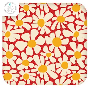 May include: A square fabric textile featuring a repeating pattern of white daisy flowers with yellow centres on a vibrant red background. The top left corner displays a circular logo with the text DELA BETA and the word home repeated around the edge.