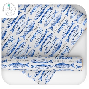 May include: White wrapping paper featuring a repeating pattern of blue sardines and the text "Sardines Lisbon Fish Market". A rolled section of the paper displays the design.