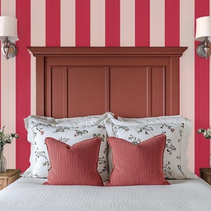 May include: A bedroom with red and white striped wallpaper, a wooden headboard, and a white bed with red pillows. The bed is made with white bedding and has two white pillows with floral patterns and two red pillows.
