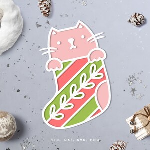 以下が含まれることがあります： 緑と赤のストライプのクリスマスストッキングから顔を出しているピンクの猫。緑の葉の模様が描かれています。EPS、DXF、SVG、PNG.