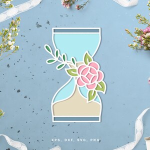 Peut inclure: Un sablier bleu avec une fleur rose et des feuilles vertes. Le sablier est sur un fond bleu clair avec de la dentelle blanche.