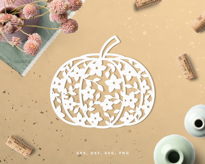 May include: White pumpkin silhouette with a floral design cut out. The pumpkin is surrounded by a light brown background with cork bottle stoppers scattered around it.
