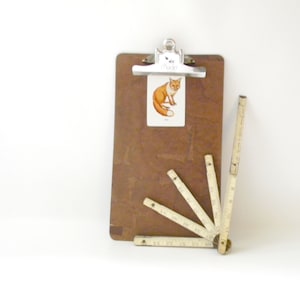 May include: A brown clipboard with a metal clip and a fox illustration on a white card. A set of five wooden folding rulers are arranged in a fan shape at the bottom of the image.