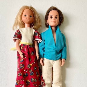 May include: A vintage doll couple, a woman with blonde hair wearing a red floral dress and a man with brown hair wearing a blue shirt and beige pants.