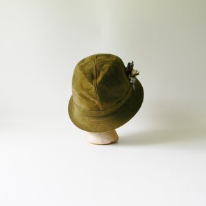 May include: A green suede bucket hat with a small floral embellishment on the side.