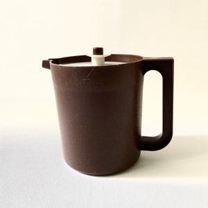 May include: A brown plastic pitcher with a white lid and a handle. The pitcher has a smooth surface and is designed for serving beverages.