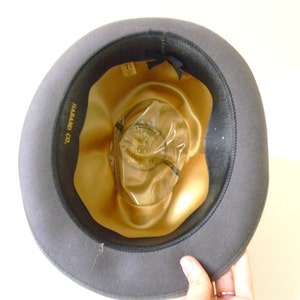 May include: A gray felt fedora hat with a gold satin lining. The hat has a label inside that reads "Harland Co."